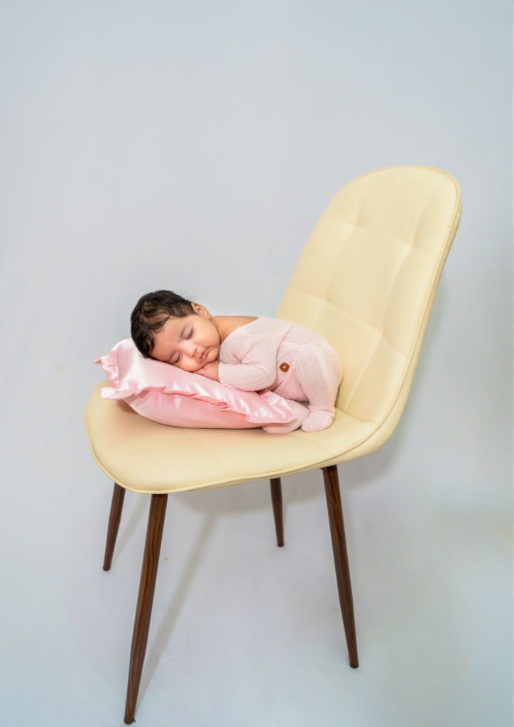 newborn baby wearing baby pink clothes sleeping on a chair