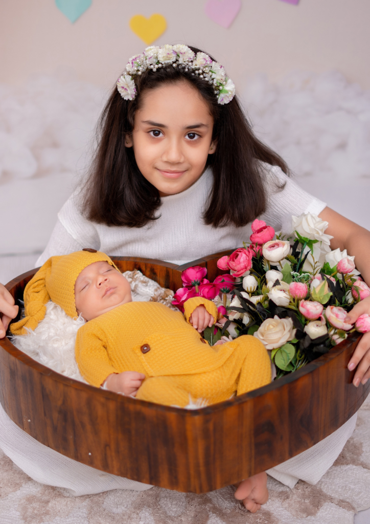 a small girl sitting holding her baby brother in her hands