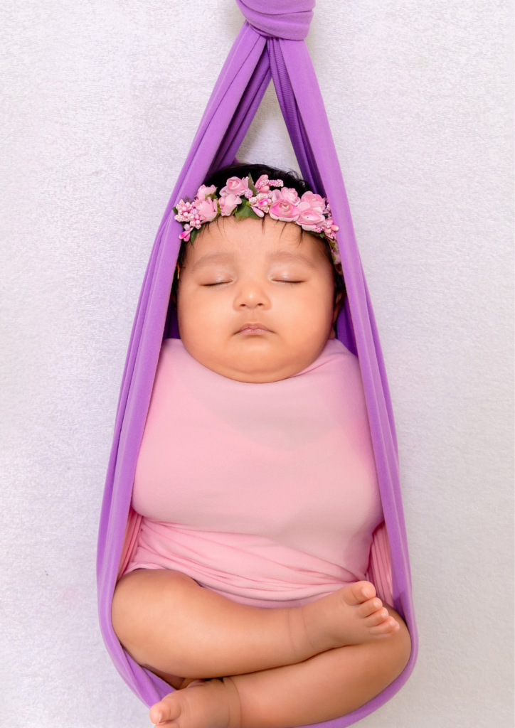 newborn baby wearing baby pink clothes hanged on a purple cloth