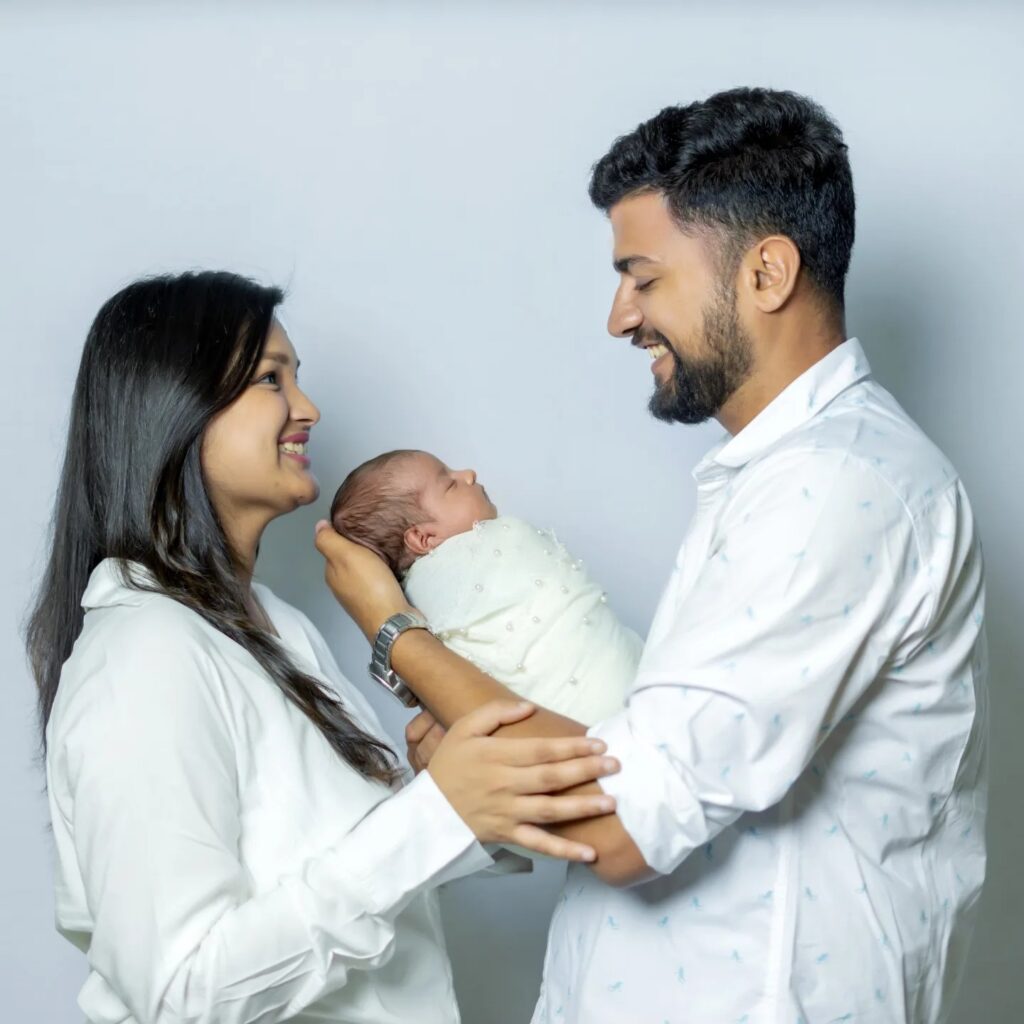 a father holding his baby in his hand and the mother supporting him with her hands